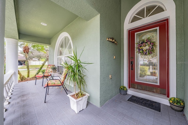 doorway to property featuring covered porch and stucco siding