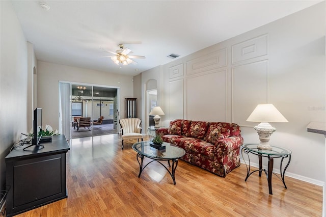 living area with light wood-style floors, a ceiling fan, arched walkways, and baseboards