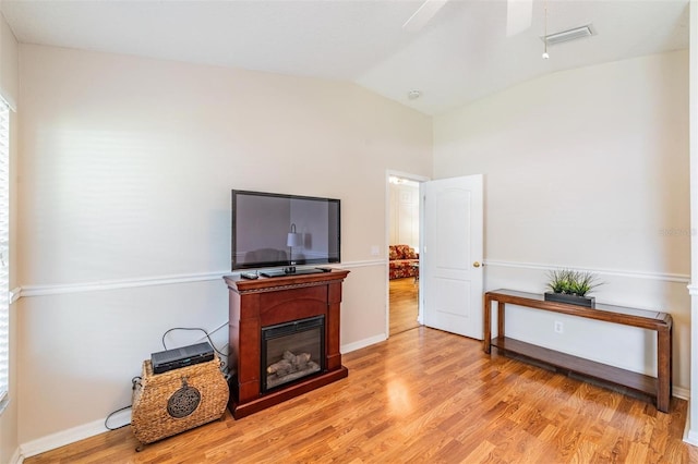 living room with light wood-type flooring, lofted ceiling, ceiling fan, a glass covered fireplace, and baseboards
