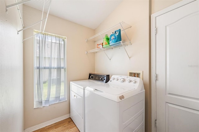 clothes washing area featuring washing machine and dryer, baseboards, and light wood-style floors