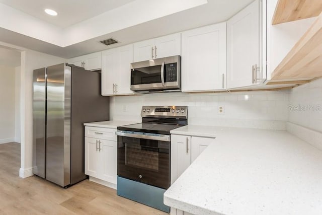 kitchen with stainless steel appliances, white cabinetry, light wood-type flooring, tasteful backsplash, and light stone counters