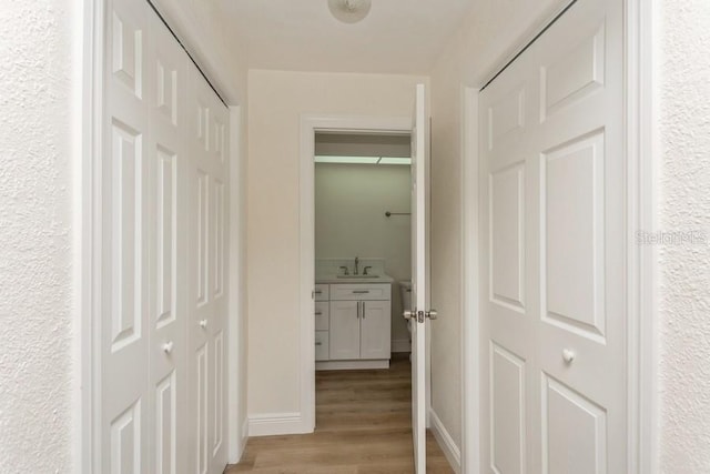 hall featuring a sink, light wood finished floors, and baseboards