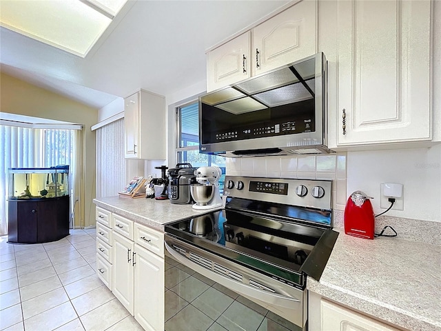 10520 Tapestry Dr, Port Richey, FL 34668 - kitchen with appliances with stainless steel finishes, light countertops, white cabinets, light tile patterned flooring, and vaulted ceiling