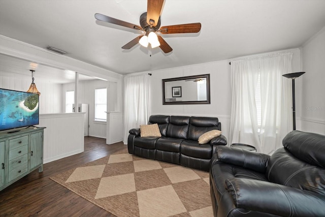 living area featuring wood finished floors, ceiling fan, wainscoting, and a decorative wall