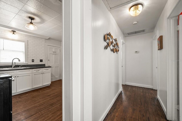 corridor with dark wood-style flooring, a sink, and baseboards