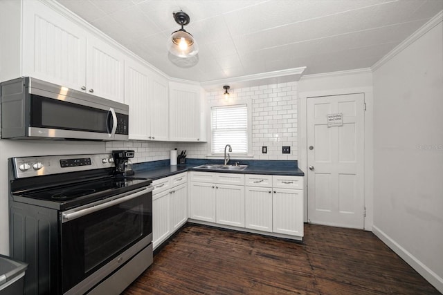 kitchen featuring appliances with stainless steel finishes, a sink, dark countertops, ornamental molding, and tasteful backsplash