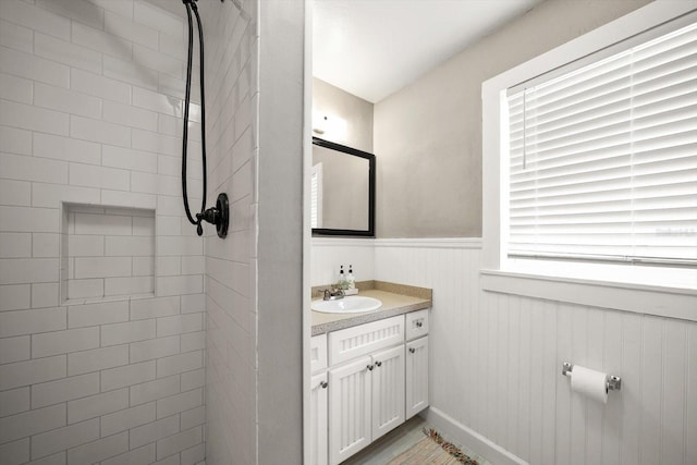 full bathroom featuring vanity, a wainscoted wall, and a tile shower