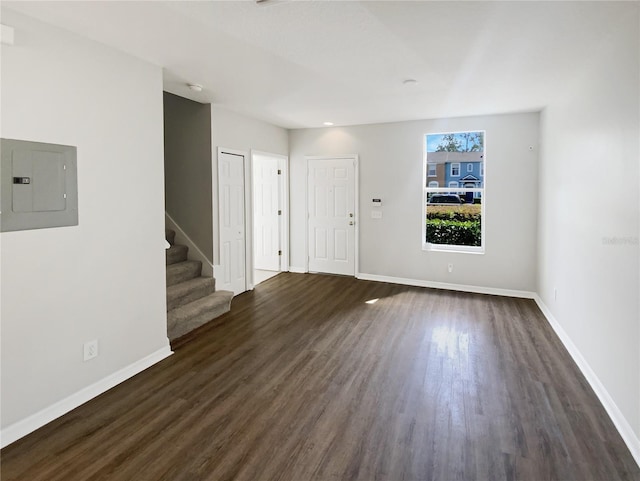 unfurnished living room with electric panel, dark wood finished floors, stairway, and baseboards