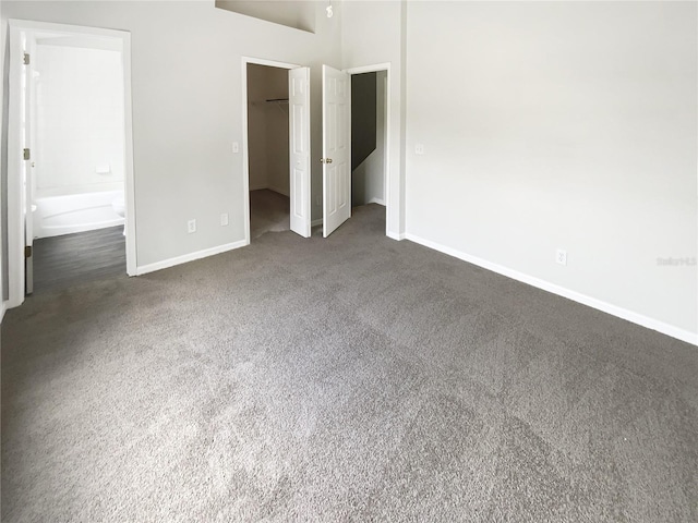unfurnished bedroom featuring baseboards, dark colored carpet, a spacious closet, a closet, and connected bathroom