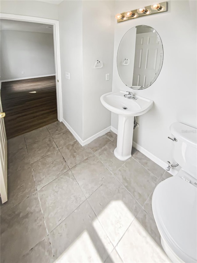 half bathroom with toilet, baseboards, and tile patterned floors
