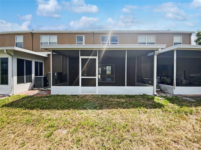 rear view of property featuring a sunroom, central air condition unit, a yard, and stucco siding