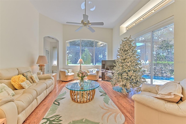 living area featuring wood finished floors, arched walkways, a ceiling fan, and a towering ceiling