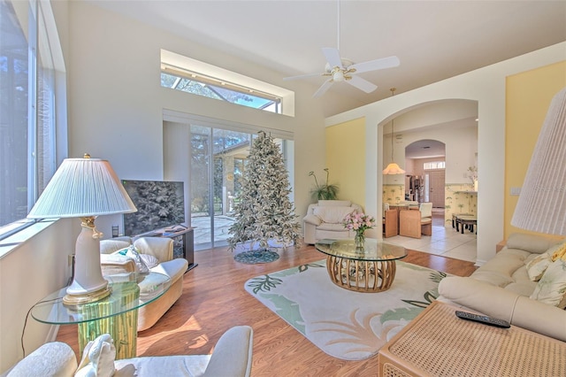 living area featuring ceiling fan, wood finished floors, arched walkways, and a high ceiling