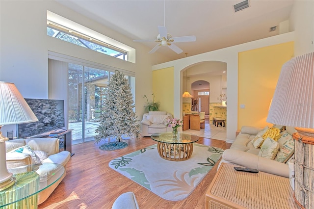 living room featuring arched walkways, wood finished floors, a ceiling fan, and a high ceiling