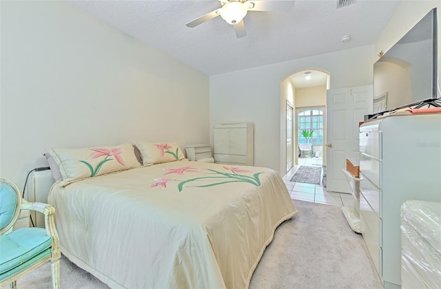 bedroom with arched walkways, light colored carpet, a ceiling fan, a textured ceiling, and light tile patterned floors
