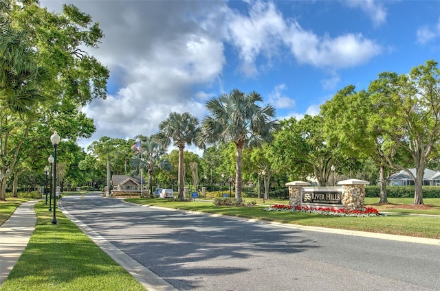 view of asphalt street featuring street lighting, curbs, and view of wooded area
