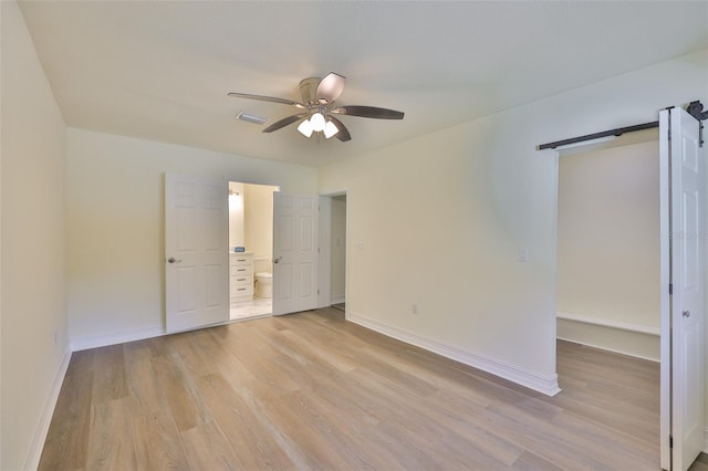 10922 Park Dr, Riverview, FL 33569 - unfurnished bedroom featuring light wood-style floors, a barn door, ensuite bathroom, and a ceiling fan