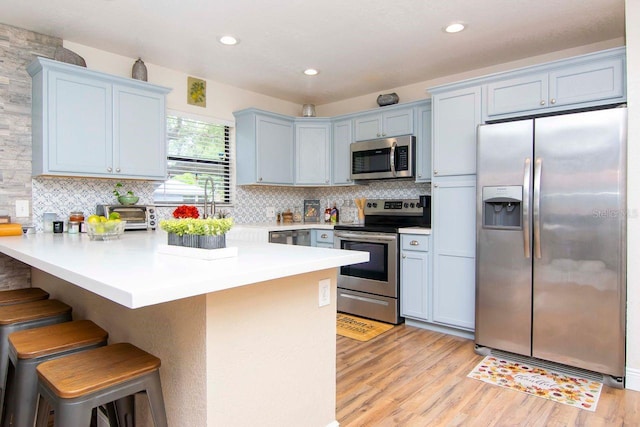 351 Hancock St, Dunedin, FL 34698 - kitchen featuring stainless steel appliances, a breakfast bar area, light wood-type flooring, tasteful backsplash, and a peninsula
