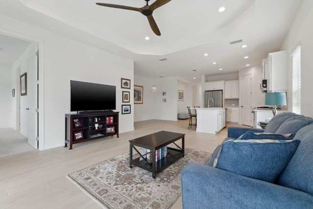 living area with a ceiling fan, light wood finished floors, recessed lighting, and a tray ceiling