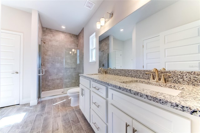 bathroom with a stall shower, toilet, double vanity, wood finished floors, and recessed lighting