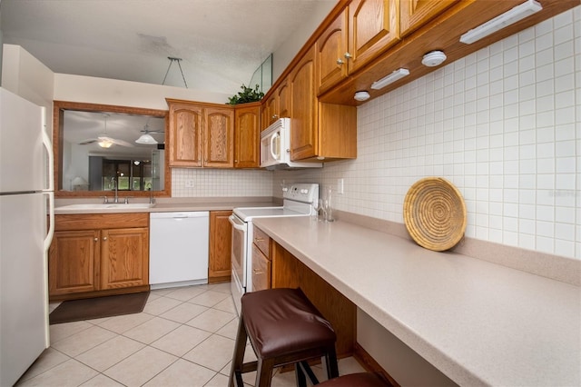 kitchen featuring white appliances, a sink, light countertops, and brown cabinets