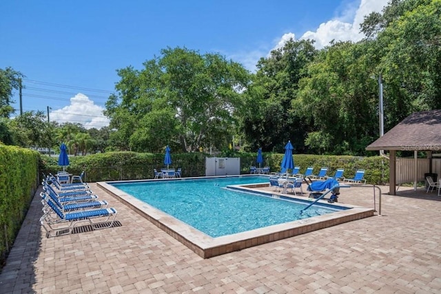 community pool with a patio, fence, and view of wooded area