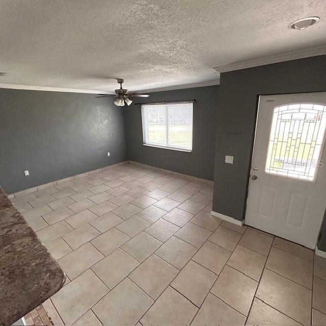foyer entrance with crown molding, ceiling fan, a textured ceiling, light tile patterned flooring, and baseboards