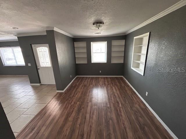 foyer featuring a textured ceiling, baseboards, ornamental molding, a textured wall, and wood finished floors