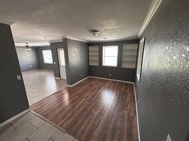 empty room with ornamental molding, a ceiling fan, a textured ceiling, tile patterned flooring, and built in shelves