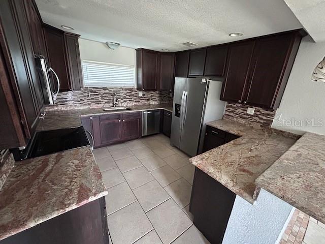 kitchen featuring stainless steel appliances, a sink, light stone counters, tasteful backsplash, and a textured ceiling