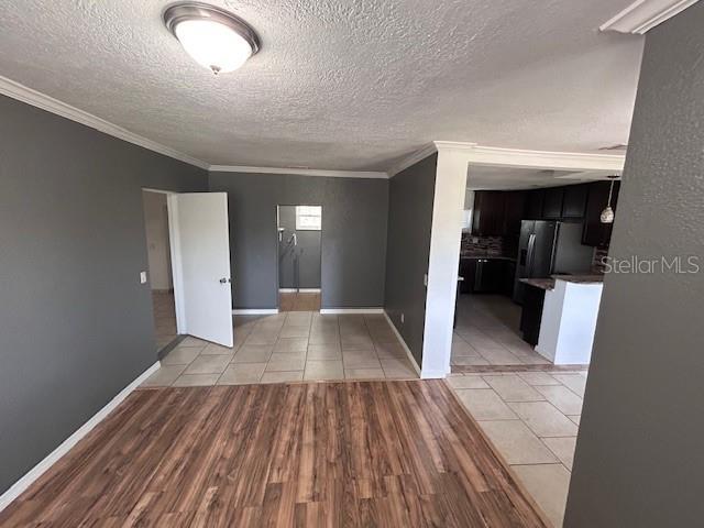 spare room featuring ornamental molding, a textured ceiling, light tile patterned flooring, and baseboards