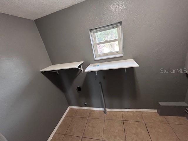 laundry area with tile patterned floors, a textured ceiling, baseboards, and electric dryer hookup