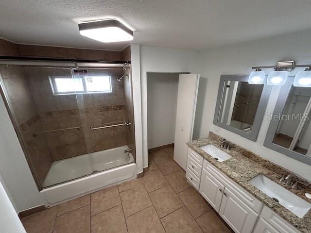 bathroom featuring tile patterned floors, a textured ceiling, double vanity, enclosed tub / shower combo, and baseboards