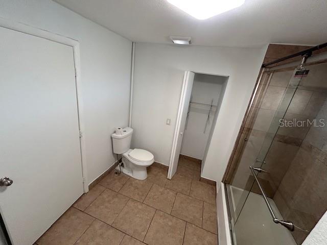 bathroom with a shower with shower door, tile patterned flooring, and toilet