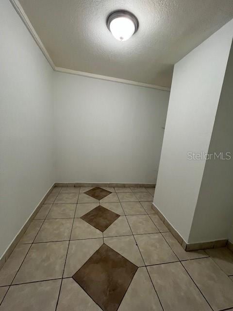 spare room featuring crown molding, a textured ceiling, baseboards, and light tile patterned floors