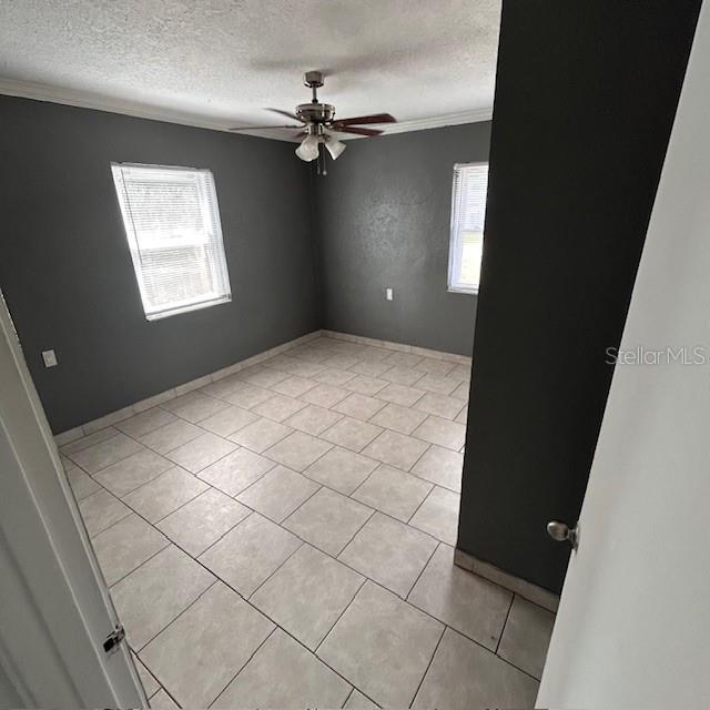 empty room with healthy amount of natural light, a ceiling fan, crown molding, a textured ceiling, and light tile patterned floors
