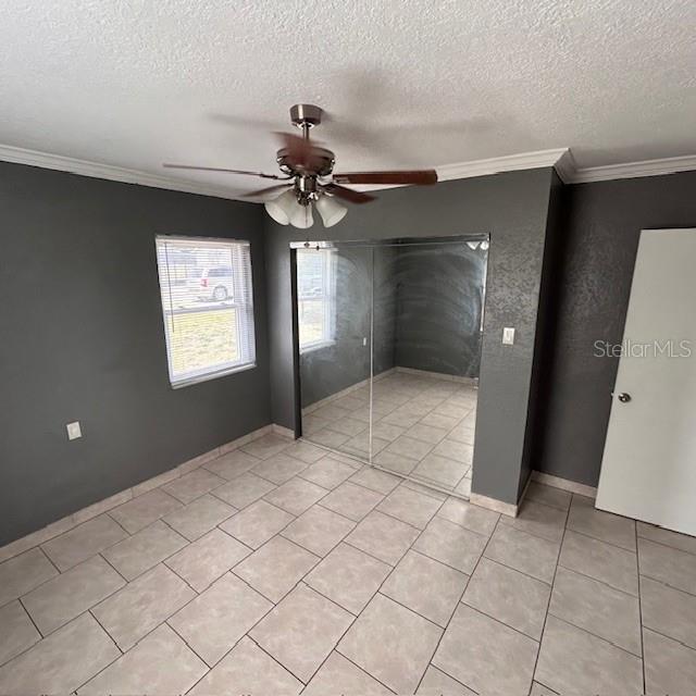 unfurnished bedroom with a textured ceiling, light tile patterned floors, crown molding, ceiling fan, and baseboards