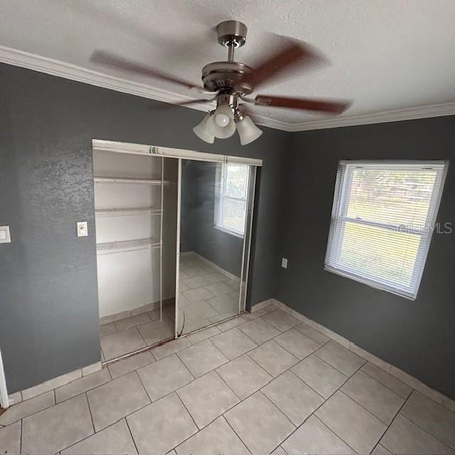unfurnished bedroom with crown molding, a closet, light tile patterned floors, a textured ceiling, and ceiling fan