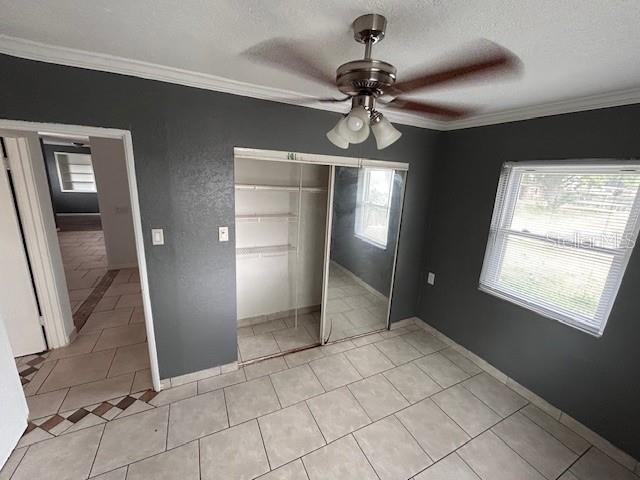 unfurnished bedroom with crown molding, a closet, a textured ceiling, light tile patterned floors, and ceiling fan