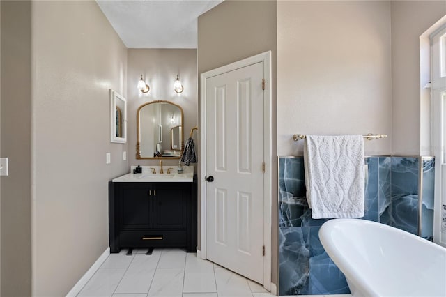 full bathroom with a soaking tub, vanity, baseboards, marble look tiles, and tile walls