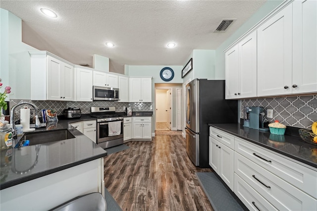 kitchen featuring stainless steel appliances, a sink, dark countertops, white cabinets, and backsplash