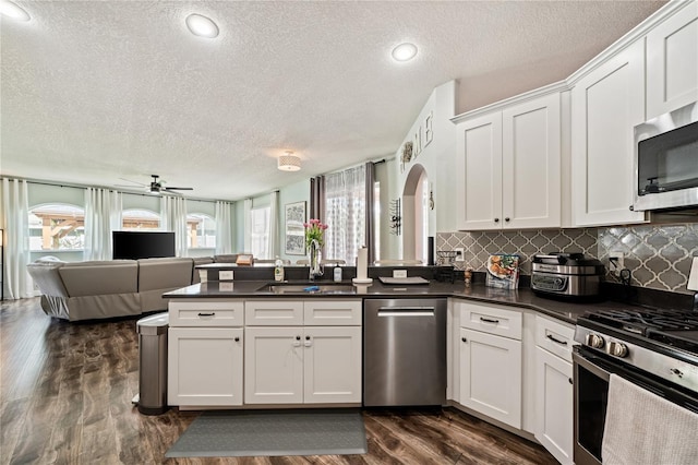 kitchen with stainless steel appliances, a sink, open floor plan, a textured ceiling, and a peninsula