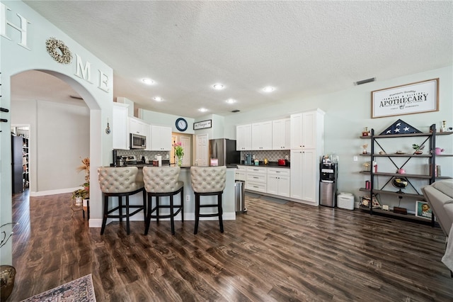 kitchen with stainless steel appliances, dark countertops, a textured ceiling, tasteful backsplash, and arched walkways