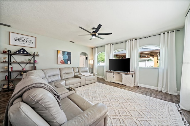 living room featuring arched walkways, wood finished floors, ceiling fan, and baseboards