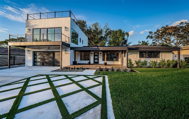 view of front of house featuring concrete driveway, a front lawn, a garage, a balcony, and stucco siding