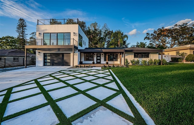view of front of house with concrete driveway, stucco siding, covered porch, a garage, and a front lawn