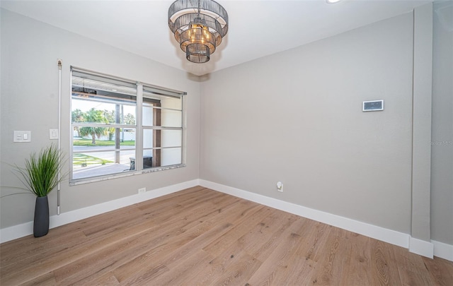 spare room with baseboards, light wood finished floors, and a chandelier