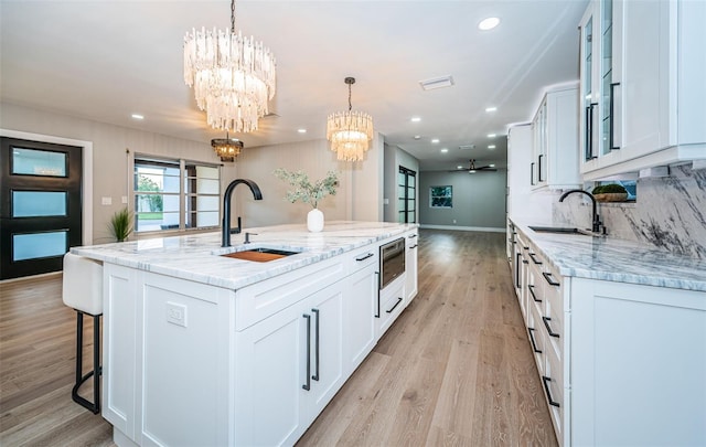 kitchen with a chandelier, a sink, light wood finished floors, light stone countertops, and recessed lighting