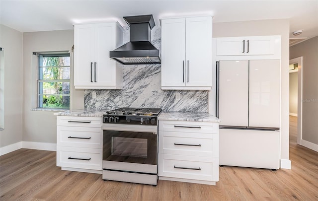 kitchen featuring range with gas stovetop, white fridge, wall chimney range hood, and baseboards