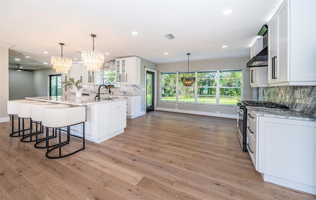 kitchen featuring stainless steel range with gas stovetop, a chandelier, a sink, wall chimney range hood, and tasteful backsplash